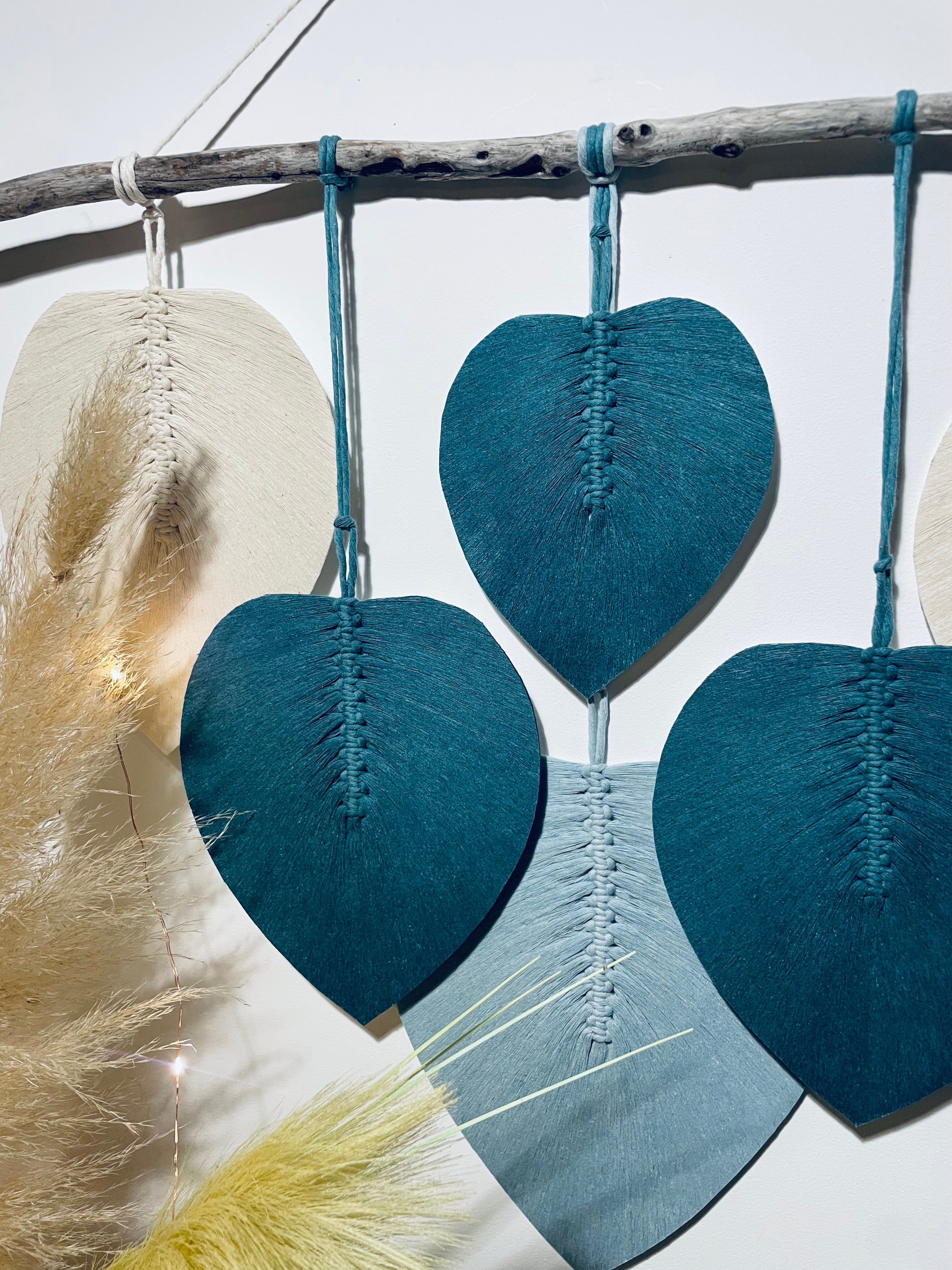 décoration murale bois flotté auquel sont suspendues des feuilles bleues claires bleues foncées et blanches en corde de coton stabilisées