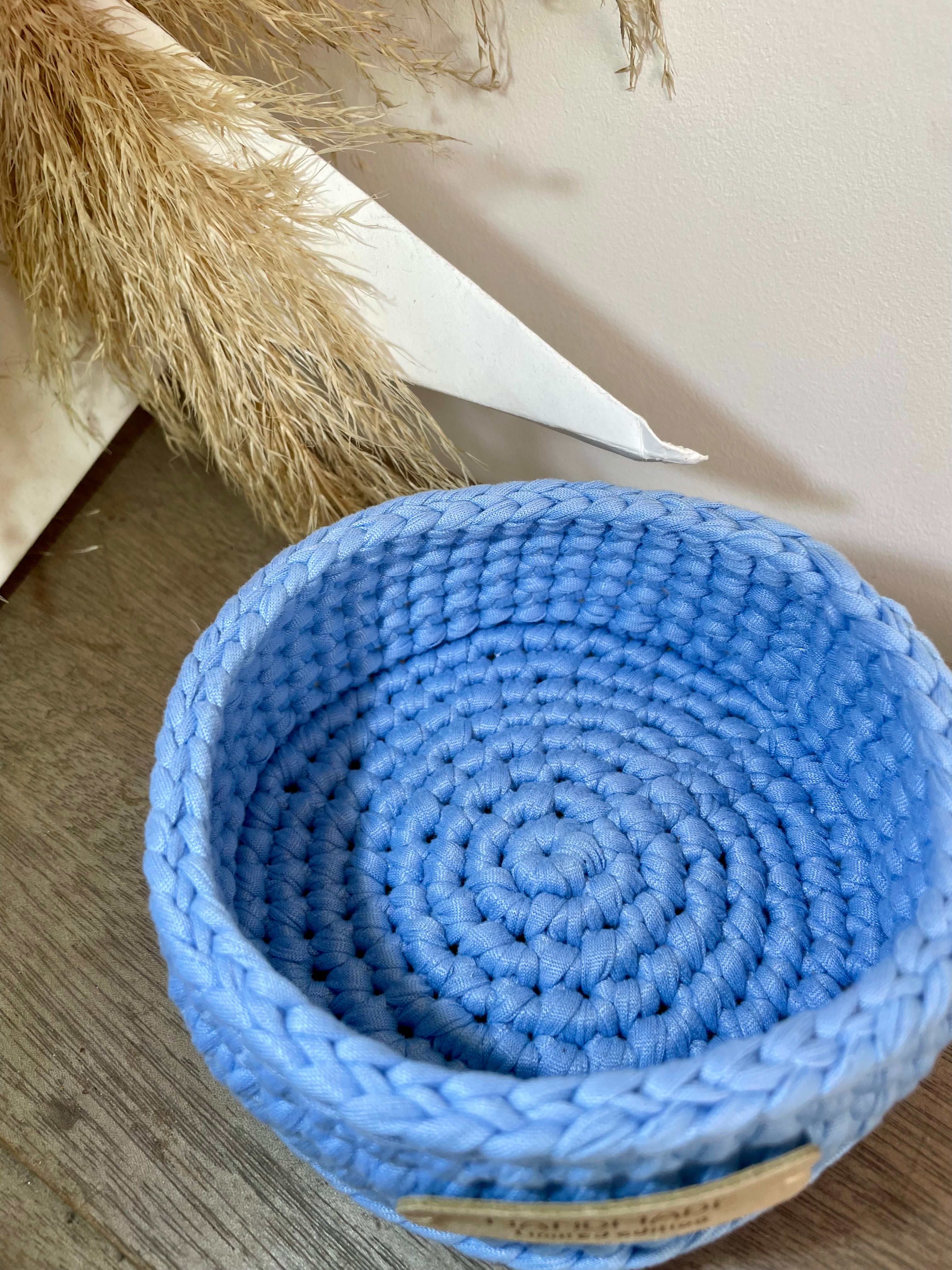 panière bleue claire fabriquée au crochet artisanalement. La panière est posée sur du bois à coté d'une décoration en papier et fleurs de la pampa
