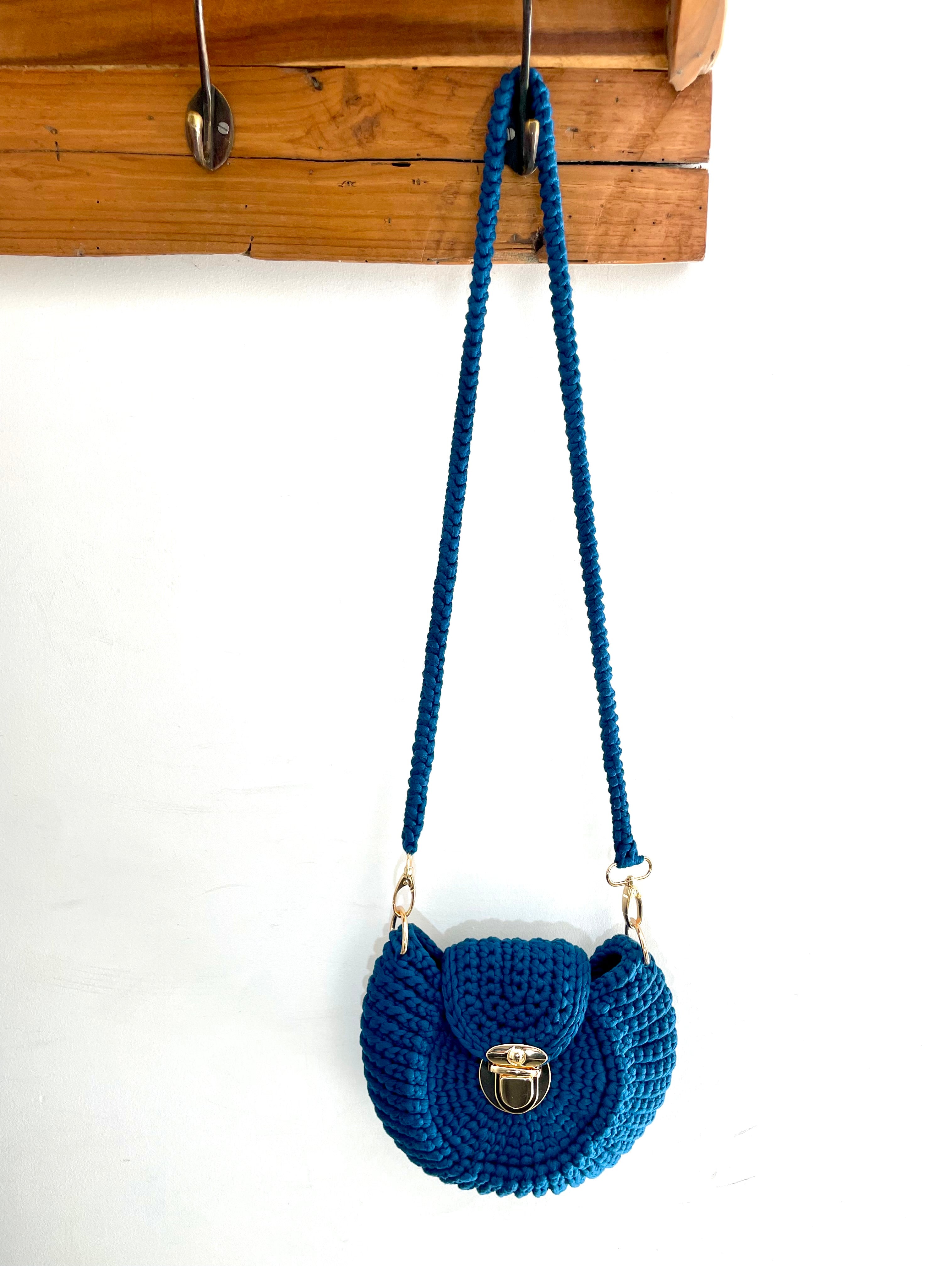sac au crochet en forme de coquillage bleu pétrole, fermoir doré. Accroché sur une patère en bois