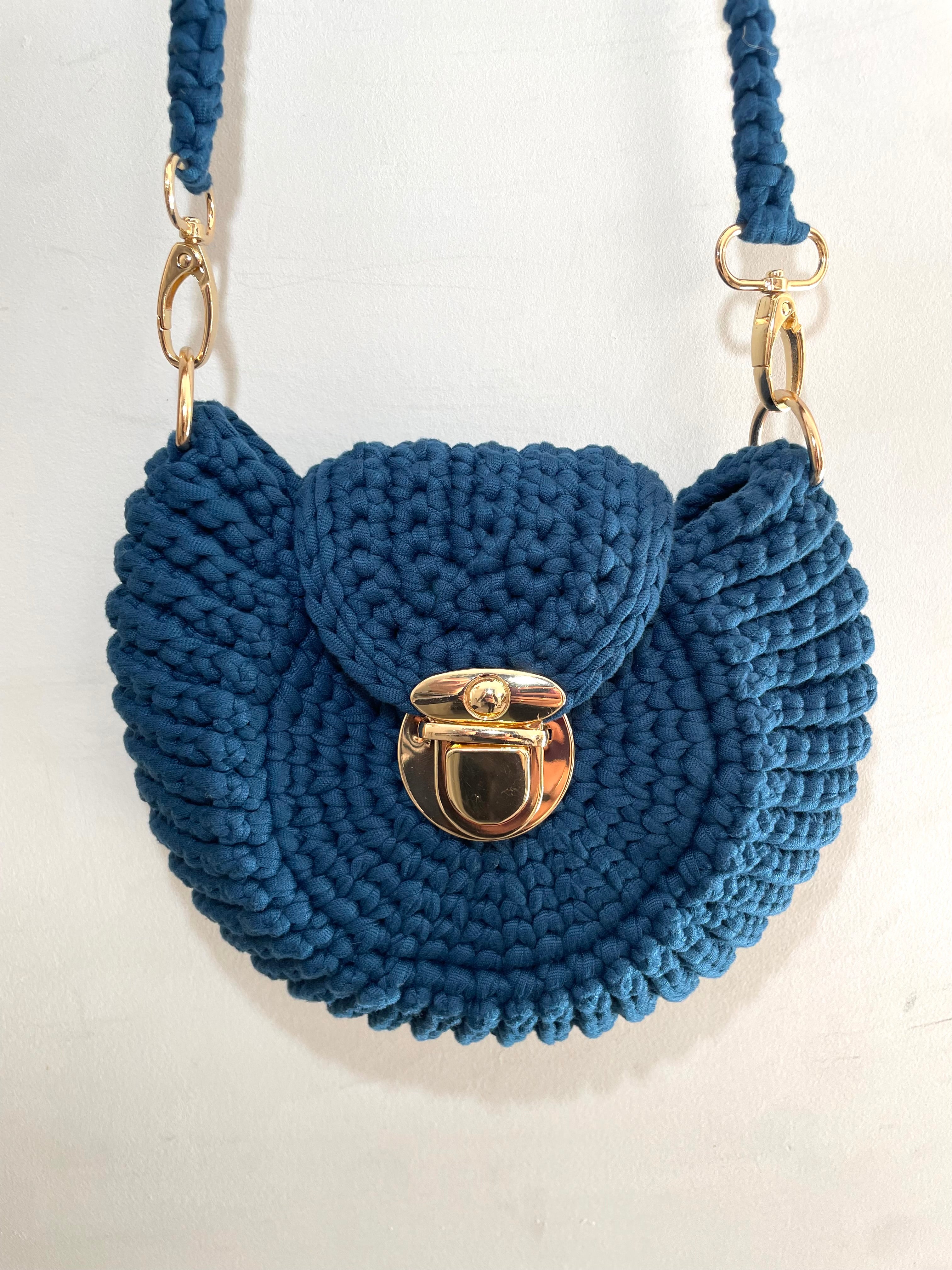 Vue de près d'un sac au crochet bleu pétrole en forme de coquillage avec des attaches dorées