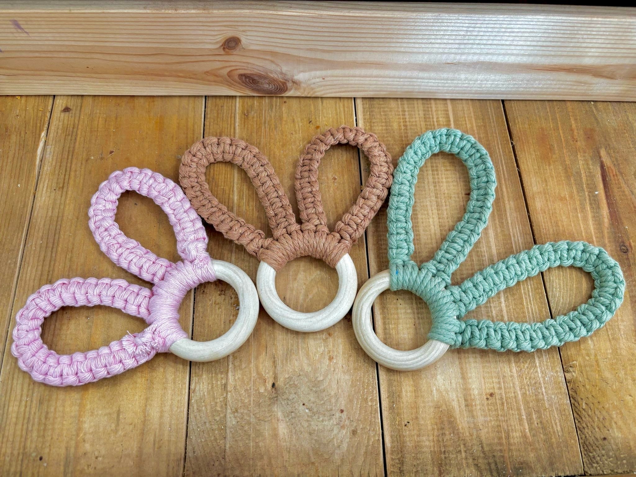 trio d'anneaux de dentitions en bois et corde de macramé en forme d'oreille de lapin un rose, un vert, un marron