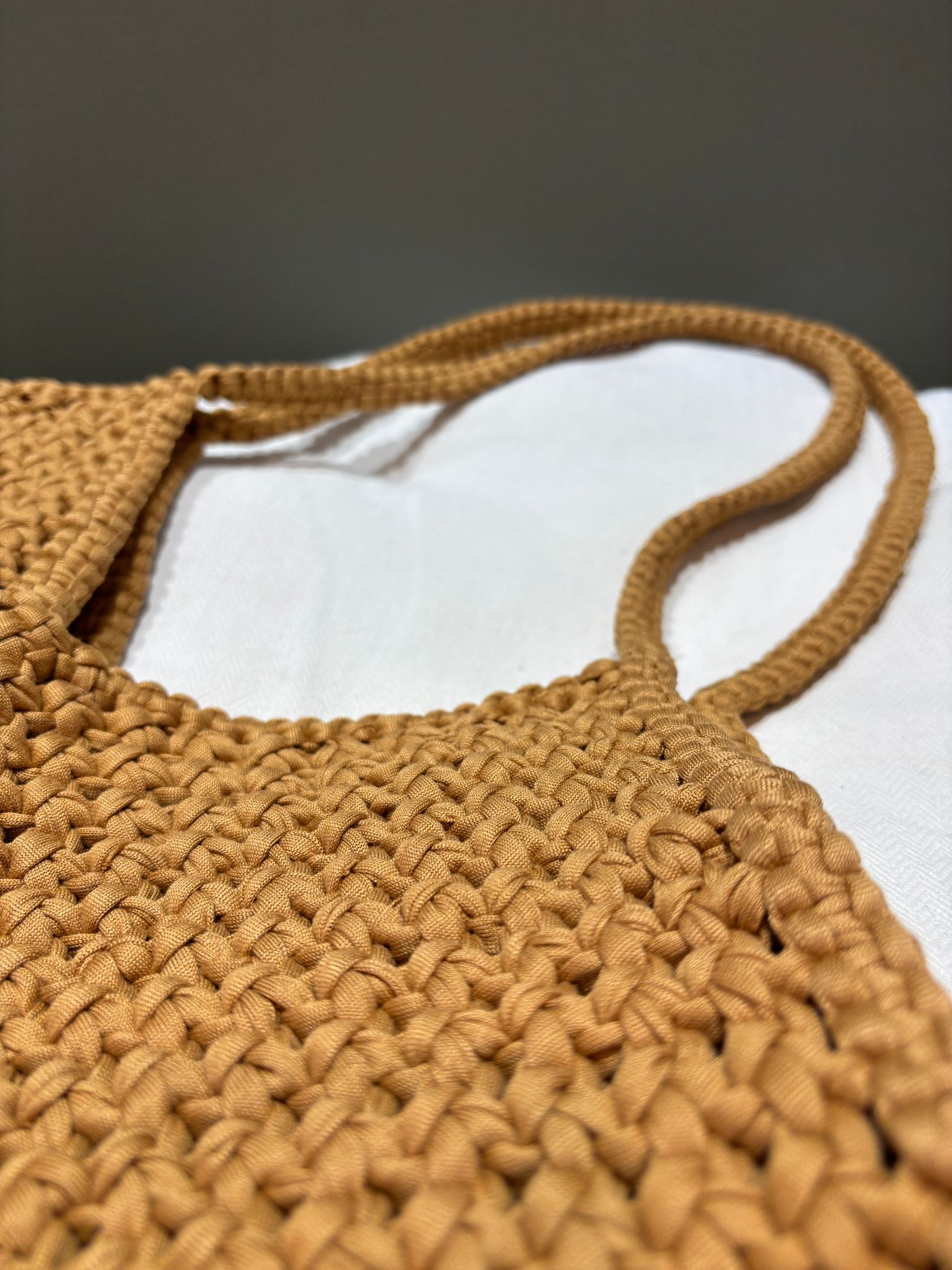 zoom sur les anses d'un sac couleur marron caramel porté épaule fabriqué avec la technique macramé. sac posé sur un tissu blanc