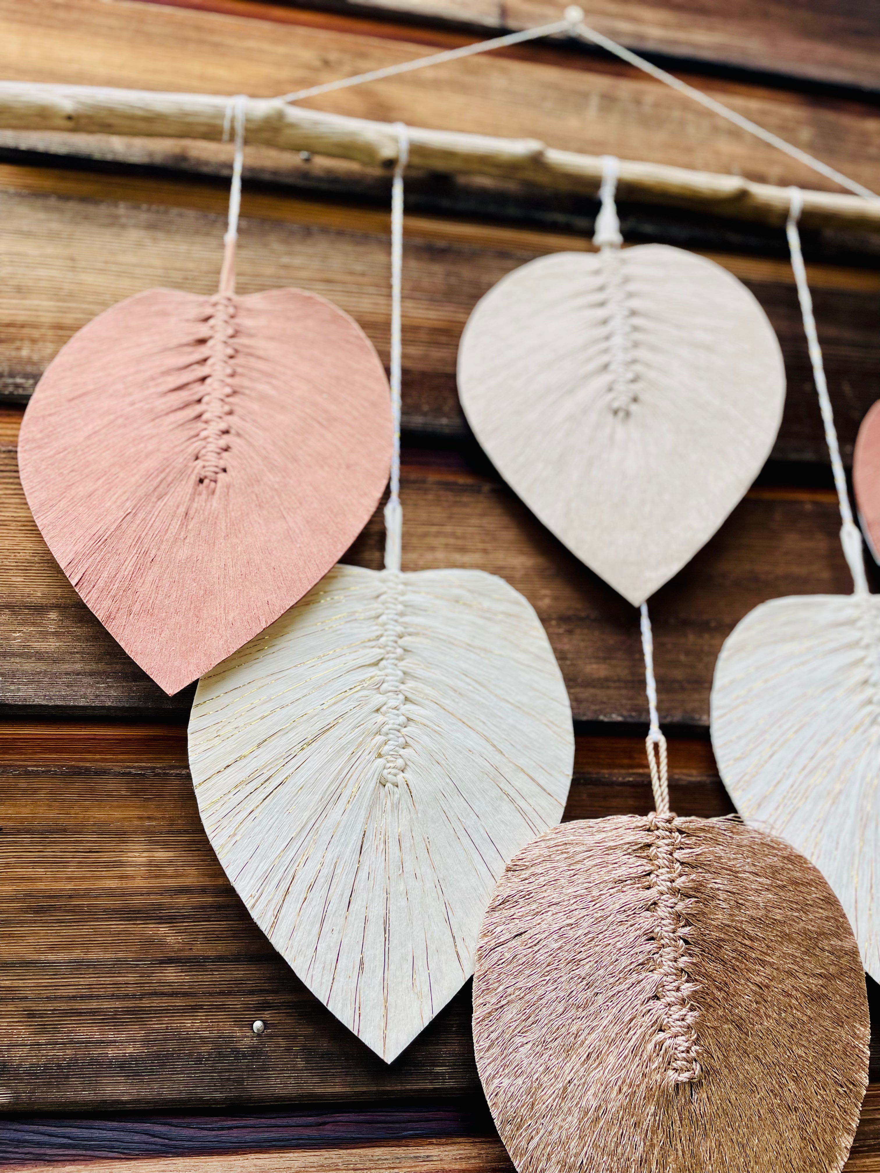 décoration murale en macramé montrant des feuilles en coton stabilisées suspendues à un bois flotté par un fil blanc et doré 