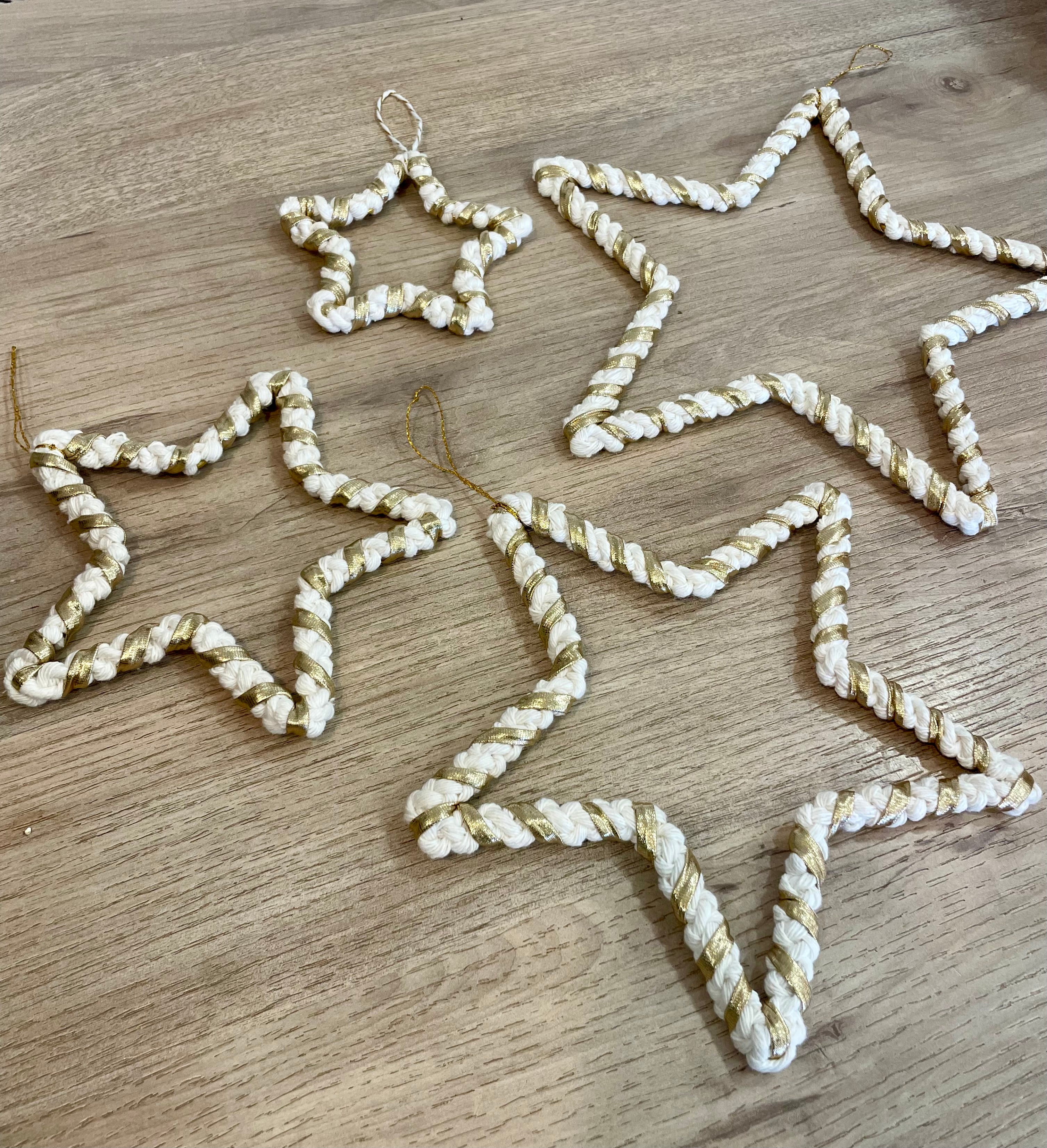 quatre décorations de tailles différentes  en forme d'étoile nouées avec la technique macramé entourées de fil doré