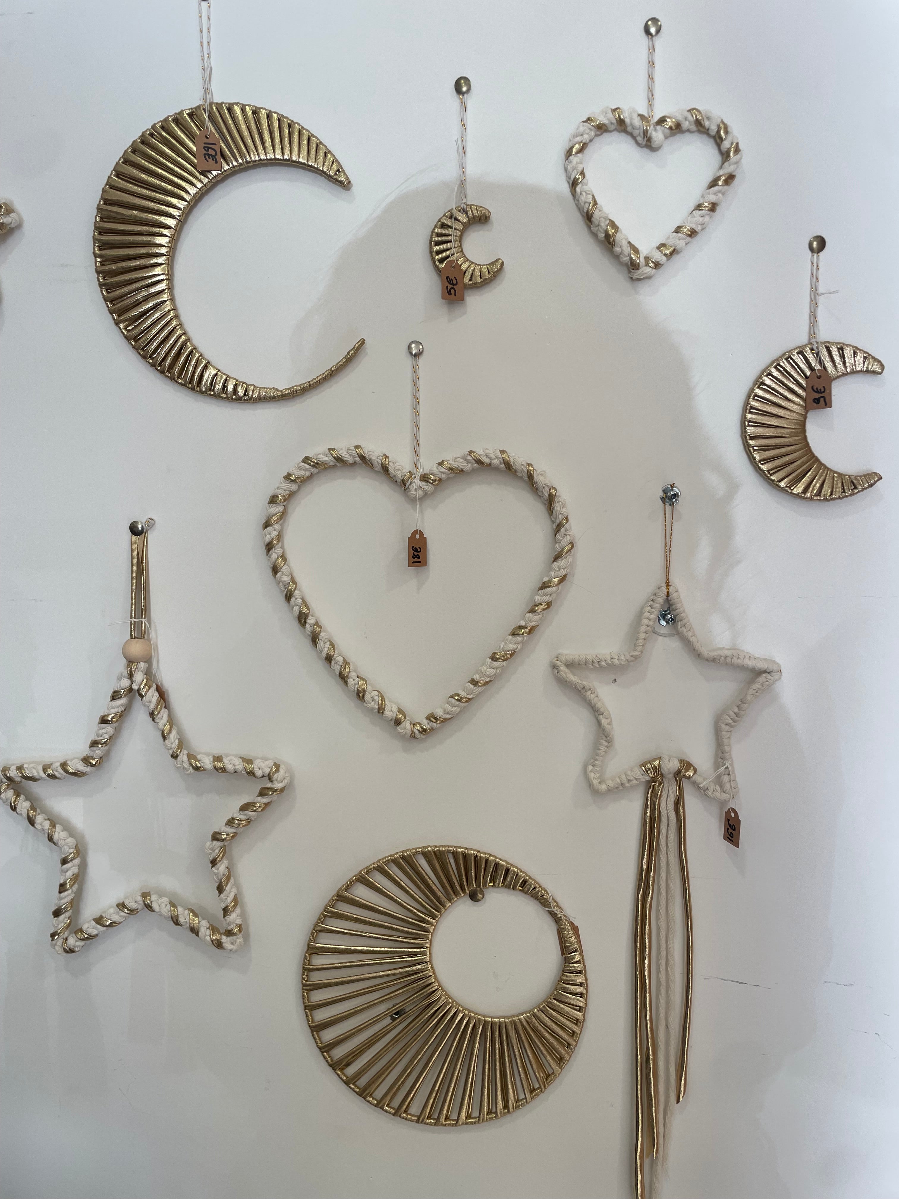 meltingpot de décorations suspendues sur un mur, fabriquées avec la technique du macramé de plusieurs formes différentes (cœurs, lunes, étoiles, soleils) couleur crème et or 