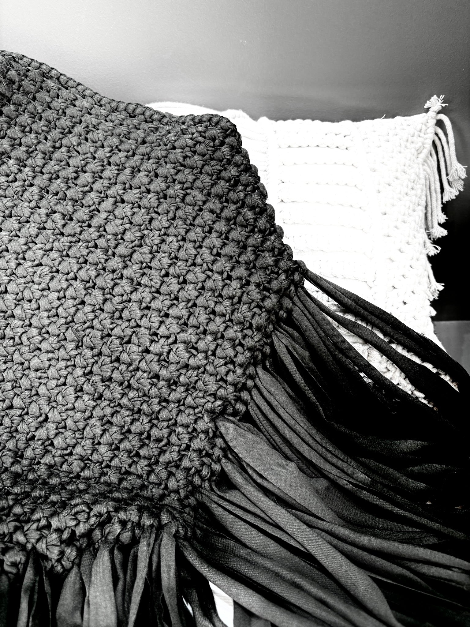 sac noir à franges tressé avec la technique macramé posé sur un coussin blanc