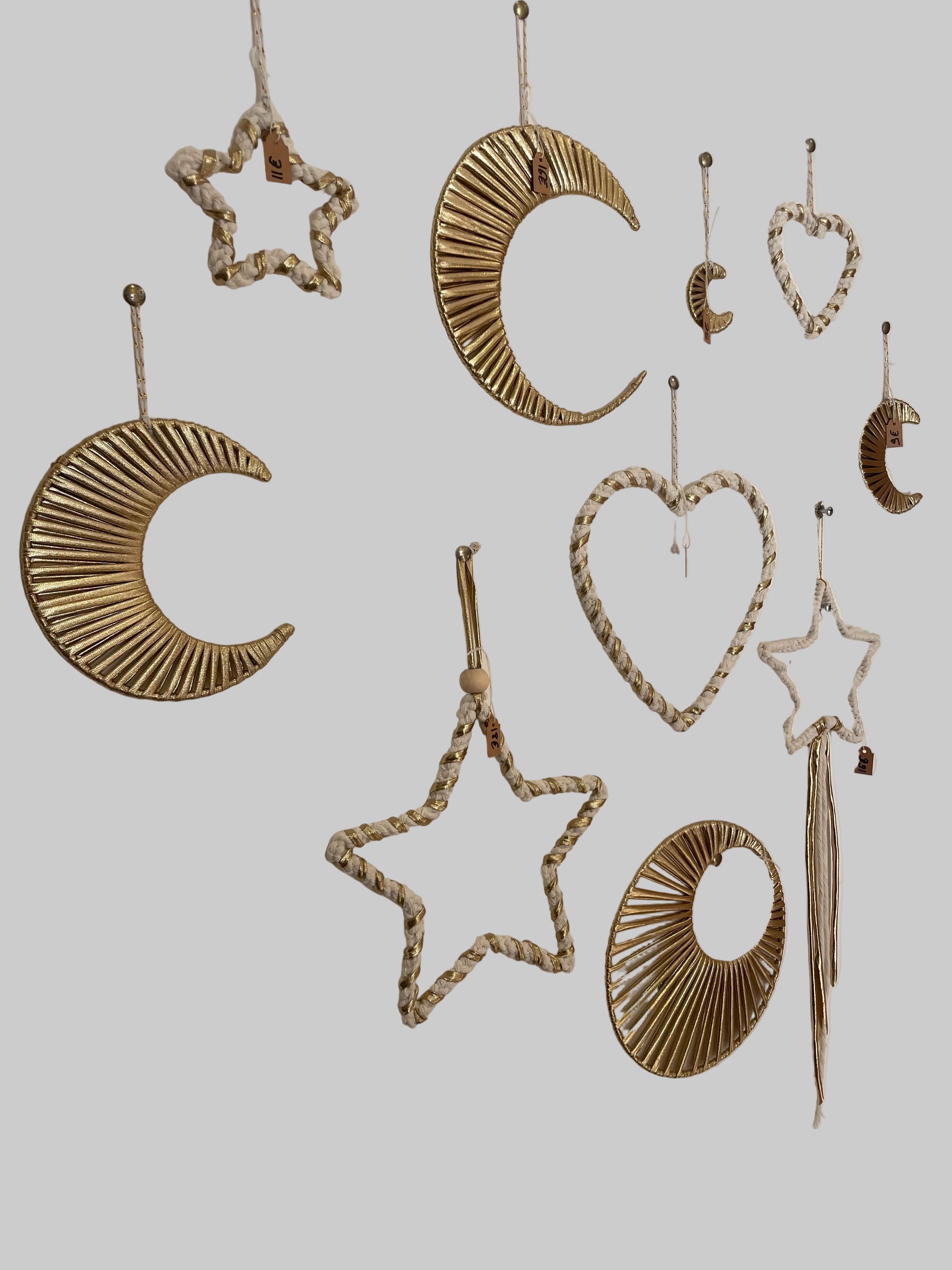 différentes décorations en macramé accrochées sur un mur. Formes de lunes, cœurs, soleils, étoiles de différentes tailles de couleur blanc et doré
