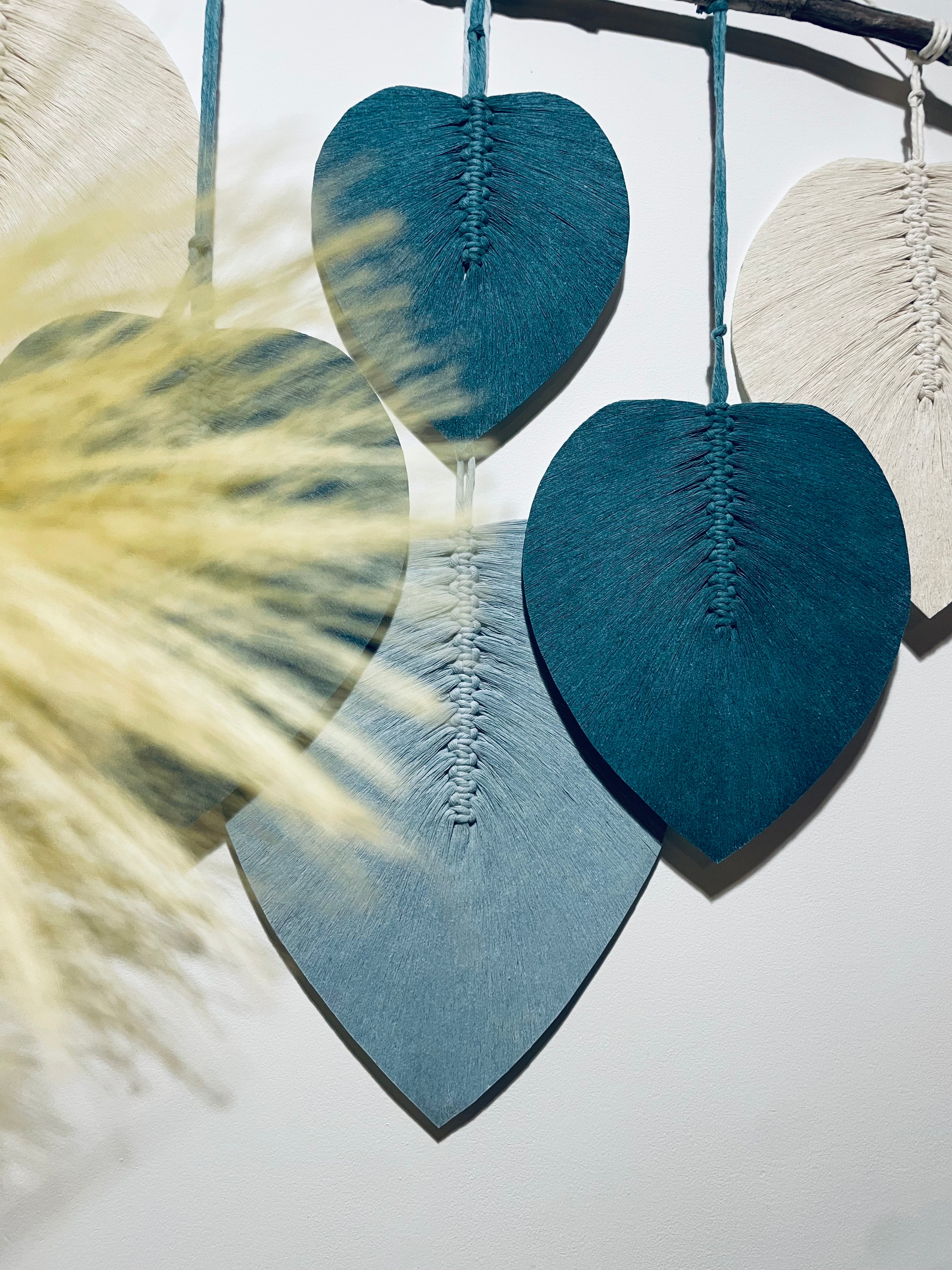 fleurs de pampa en premier plan et arrière plan des feuilles bleues stabilisées en corde de coton bleue et blanches accrochées sur un bois flotté