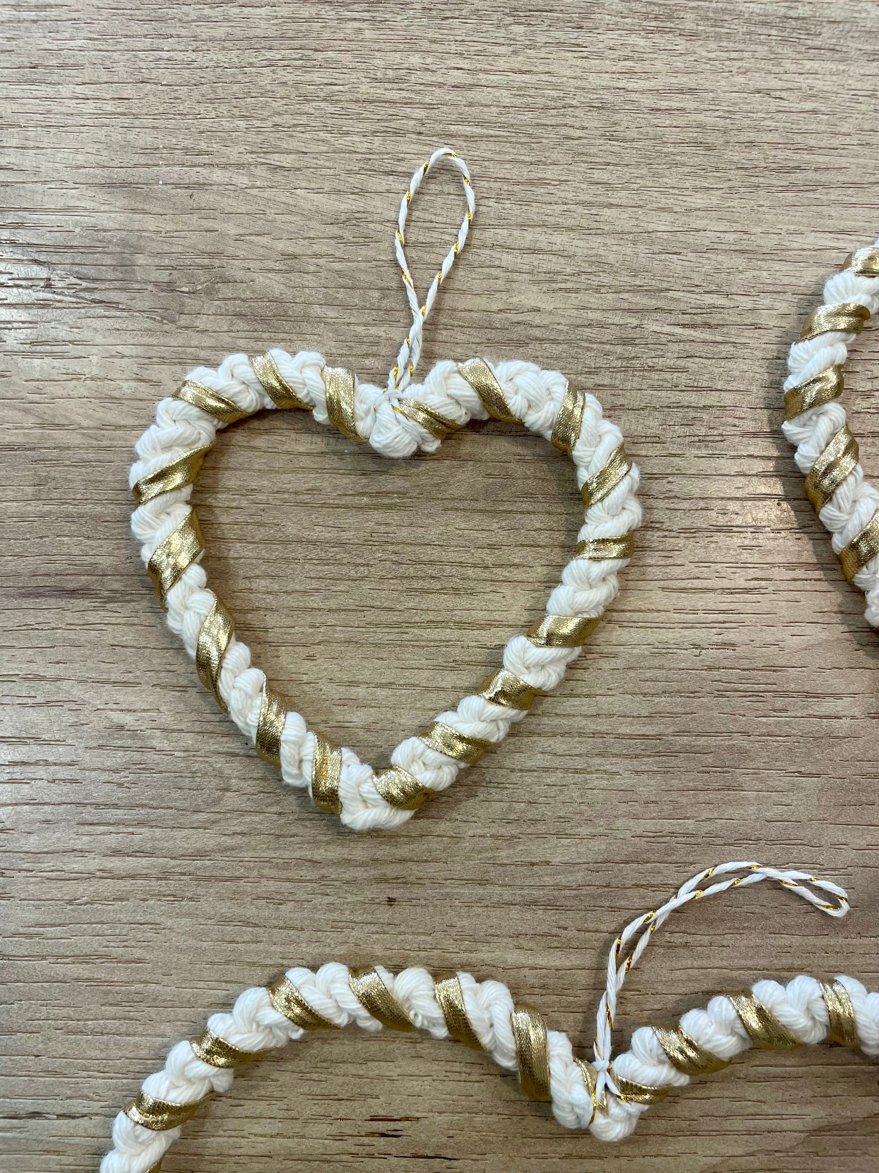 zoom sur une décoration en forme de cœur de petite taille tressé avec la technique macramé beige et or 