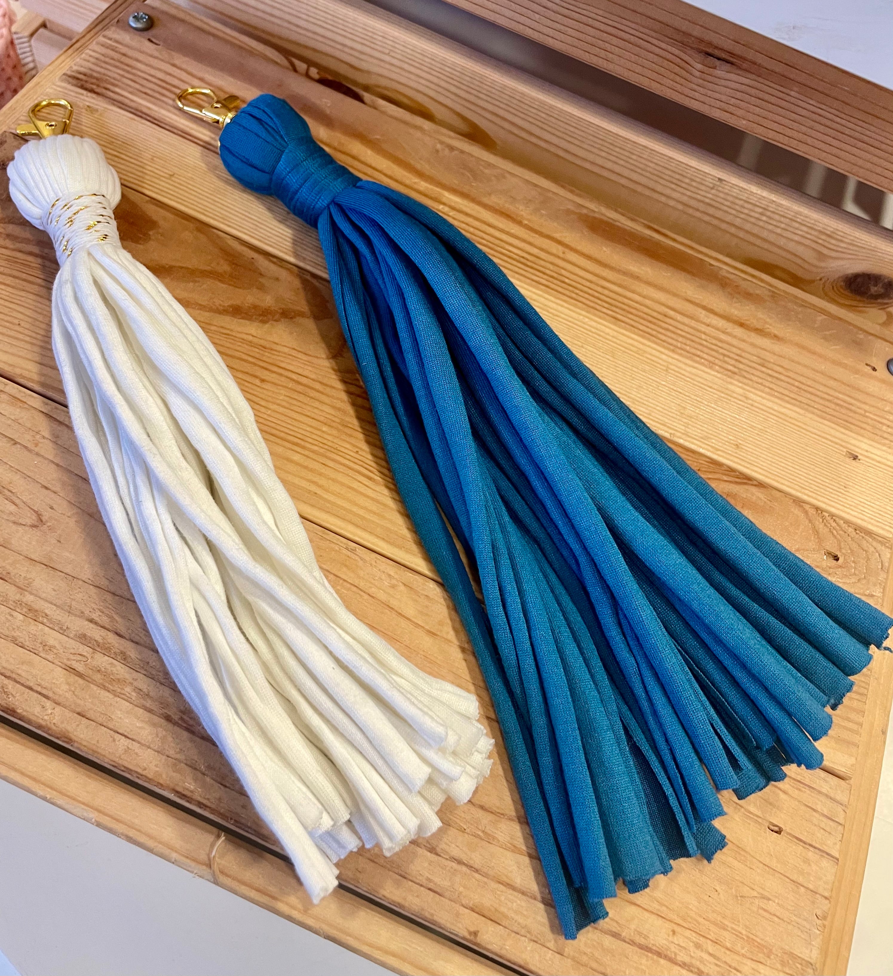 un porte-clés pompon bleu et un porte-clés blanc côte à côte les ils sont assez longs environ 10 cm