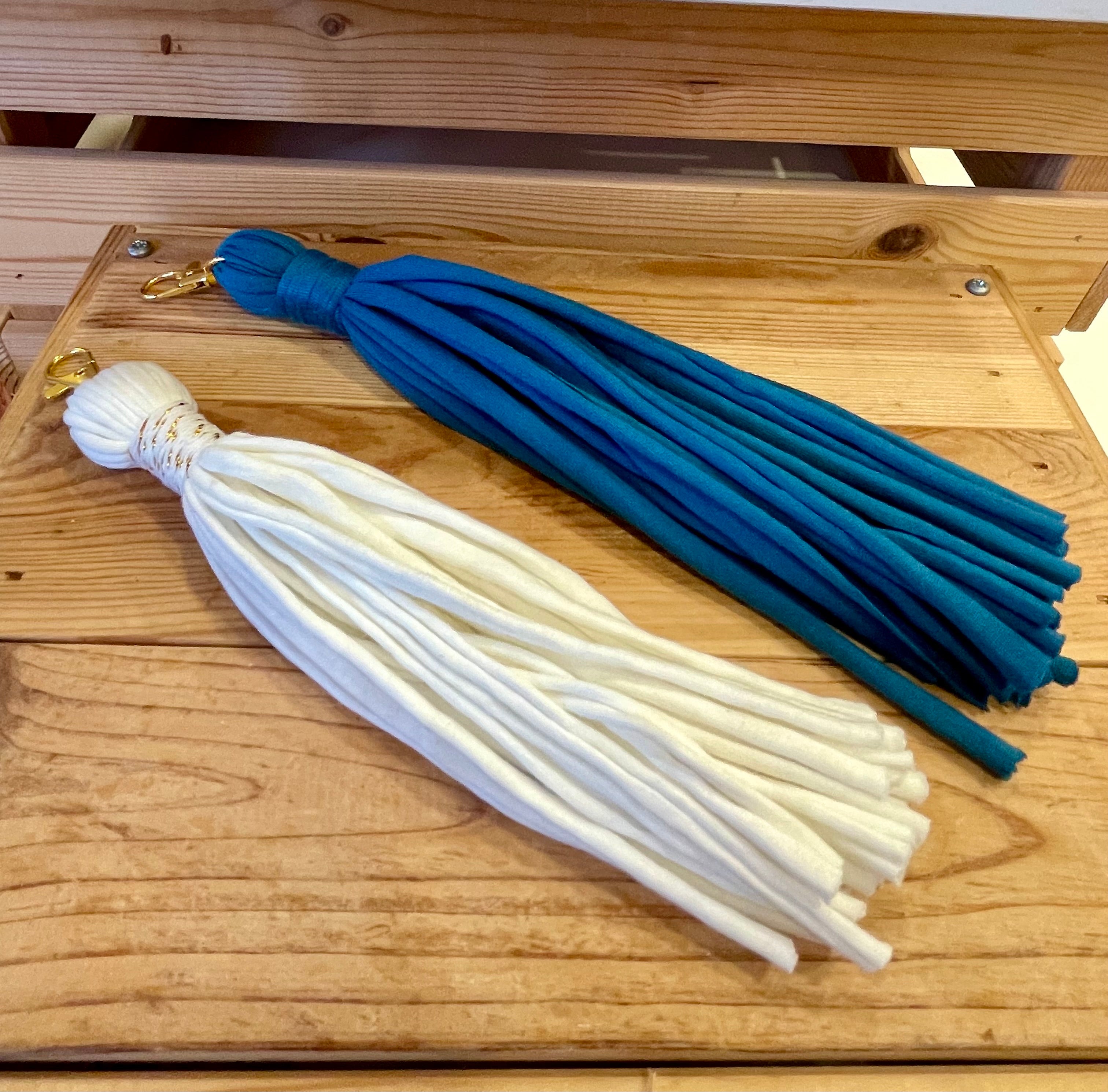 deux porte-clés pompons posés côte à côte sur du bois. Celui de gauche est blanc celui de droite est bleu