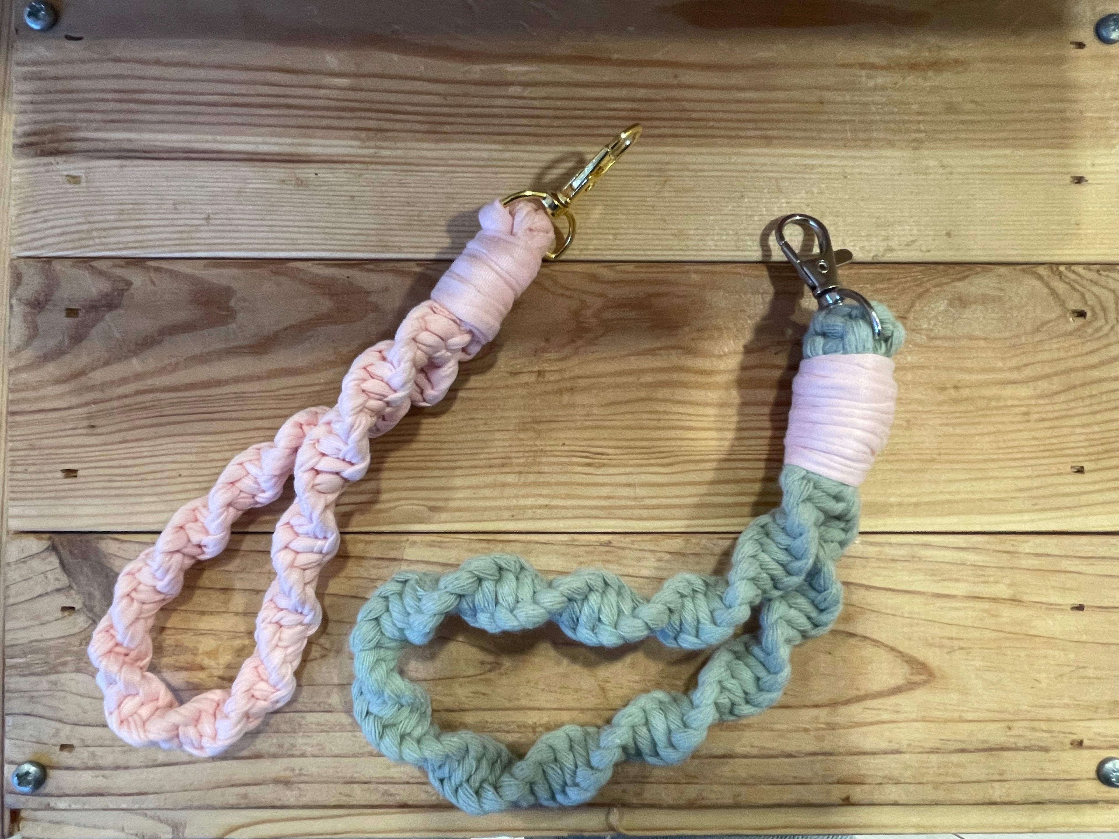 deux porte-clés posés sur du bois. Le premier est rose poudré avec une attache dorée et le deuxième est vert sauge avec une attache argenté