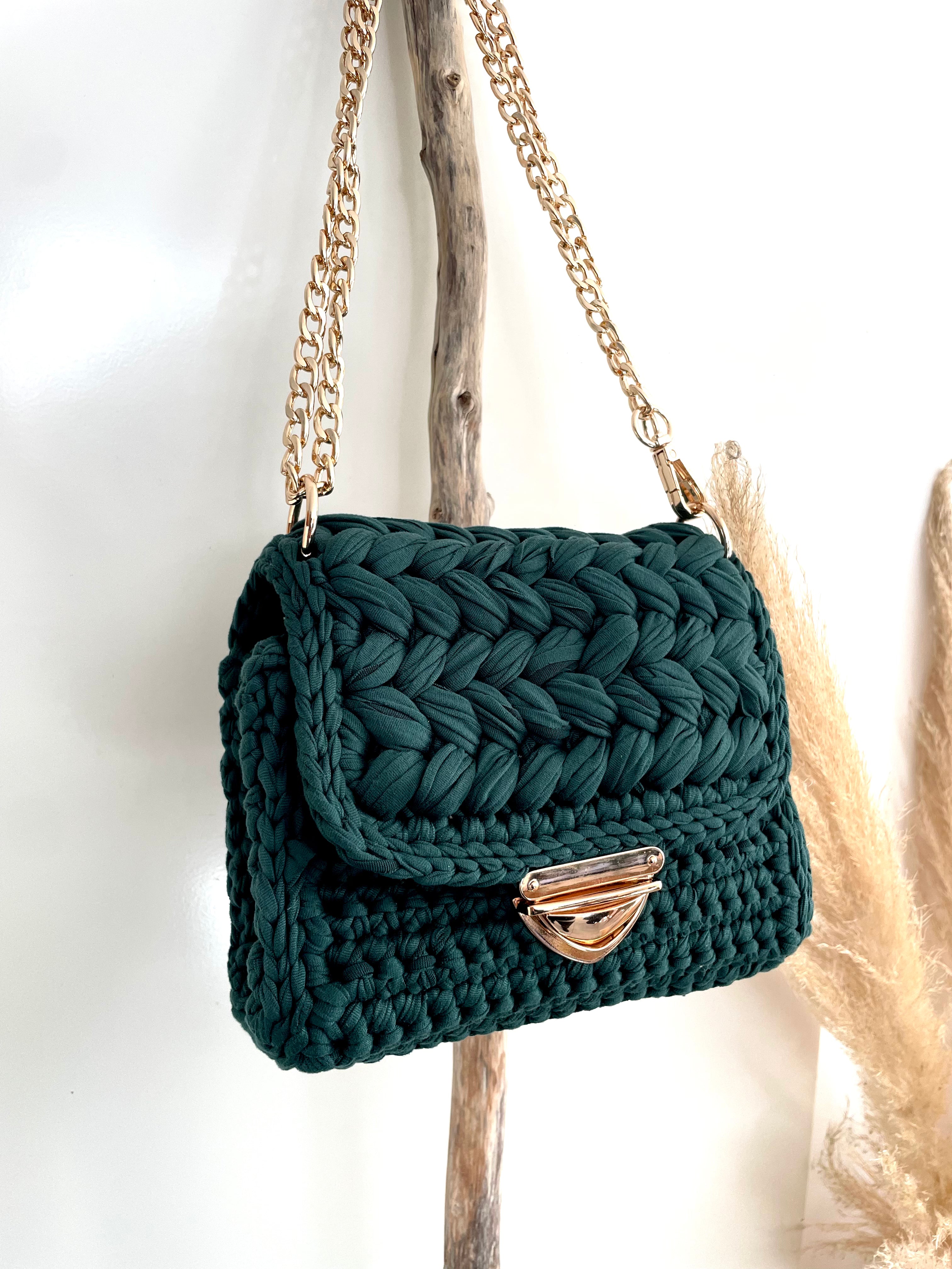 sac vert au crochet accroché par la sangle en métal doré  sur un morceau de bois