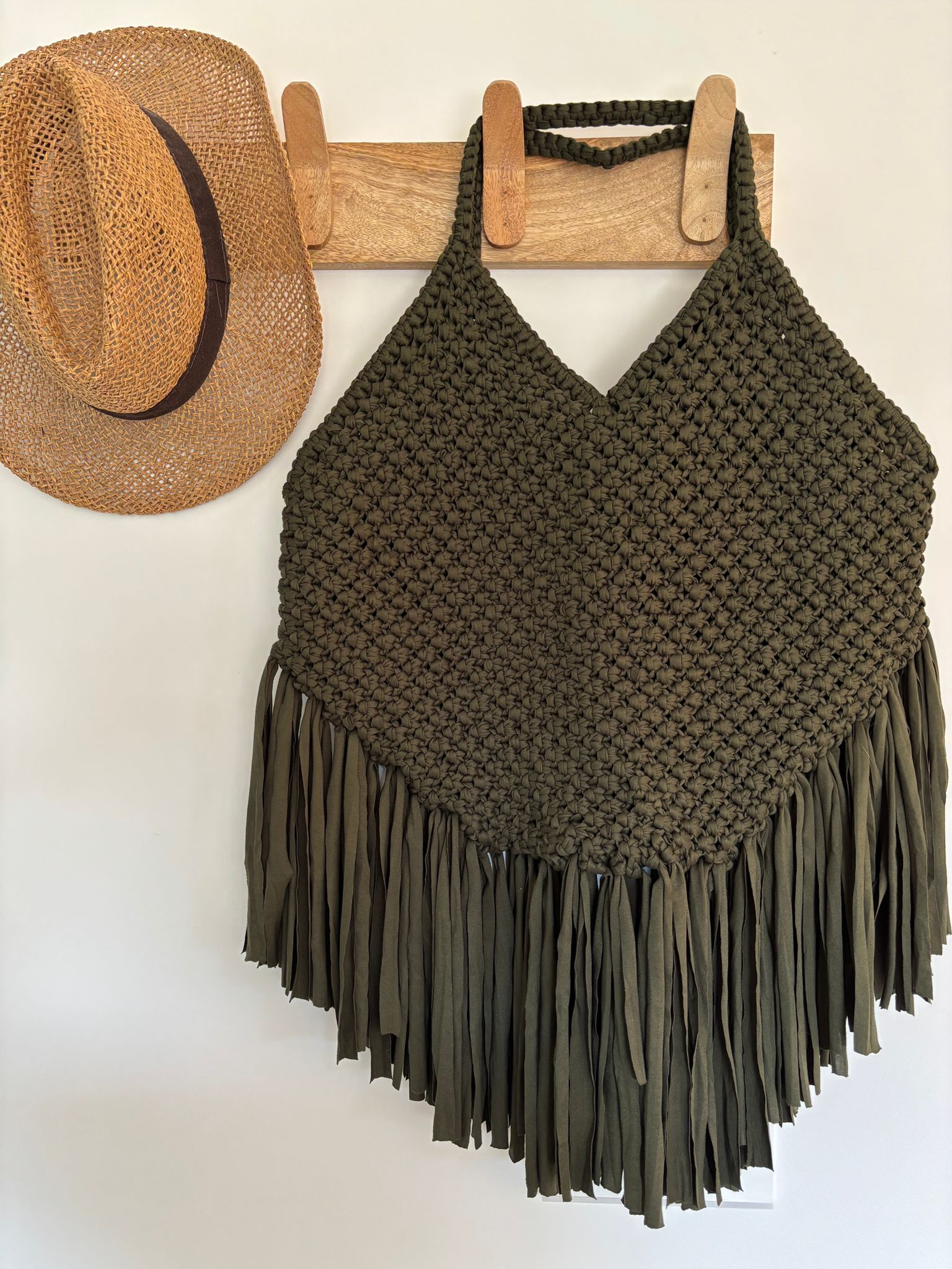sac à franges fabriqué artisanalement technique macramé de forme triangulaire, accroché sur une patère en bois à coté d'un chapeau de paille