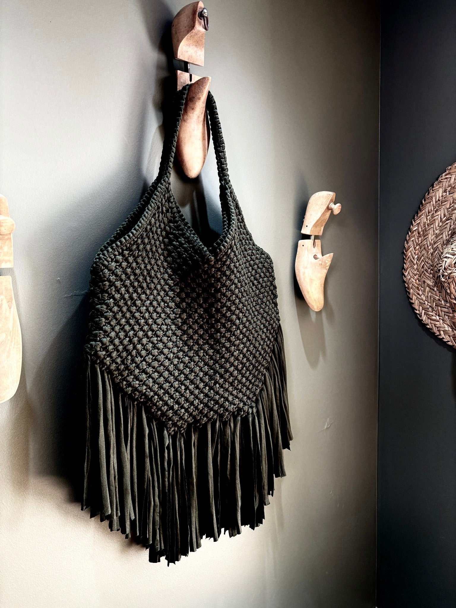 sac à franges noir fabrication artisanale en macramé taille moyenne porté épaule accroché contre un mur sur une patère en forme de chaussure