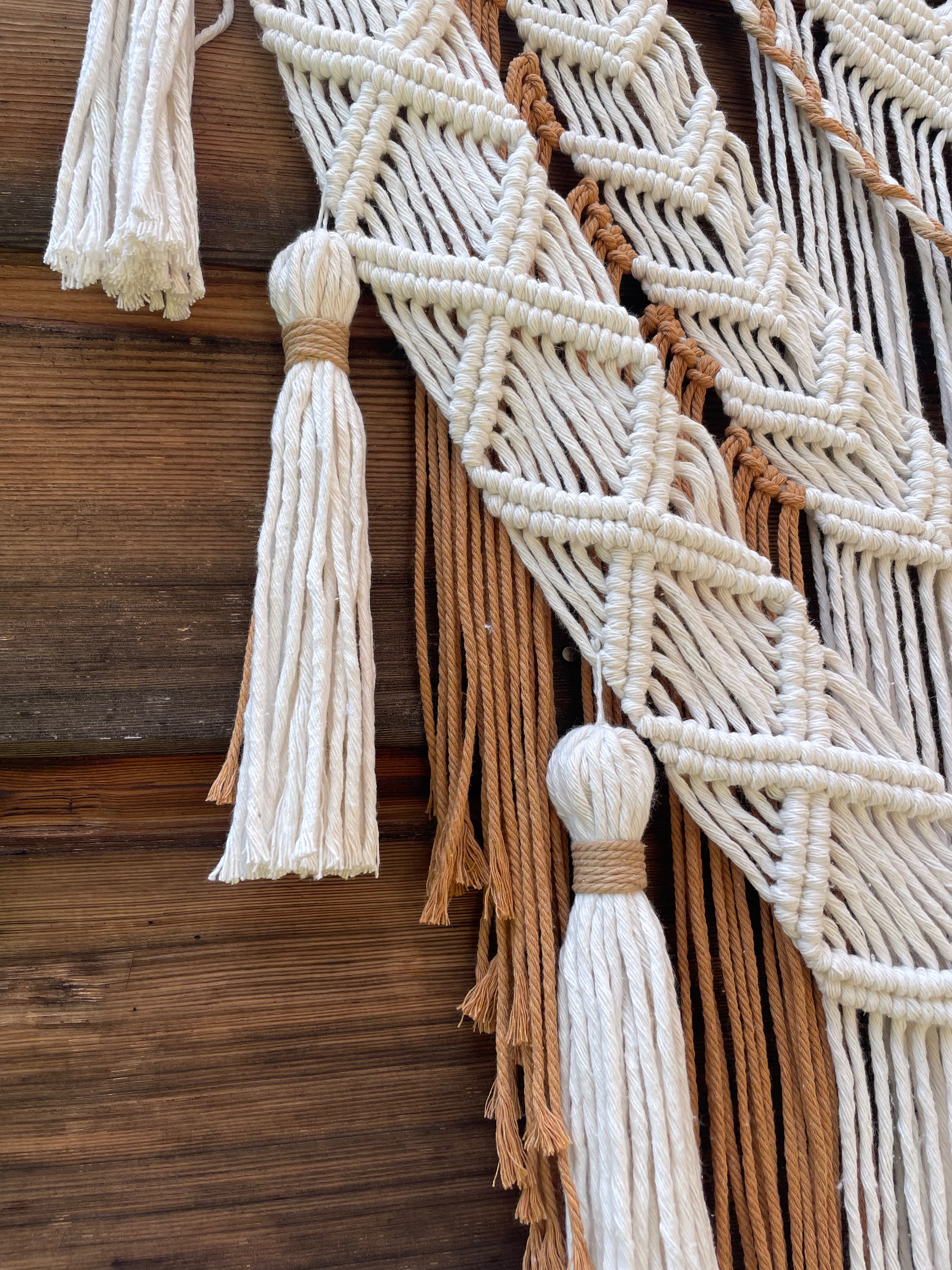 tenture murale style bohème chic couleurs blanc et marron beige fabrication artisanale avec de la corde de coton tressage méthode macramé pompons blancs