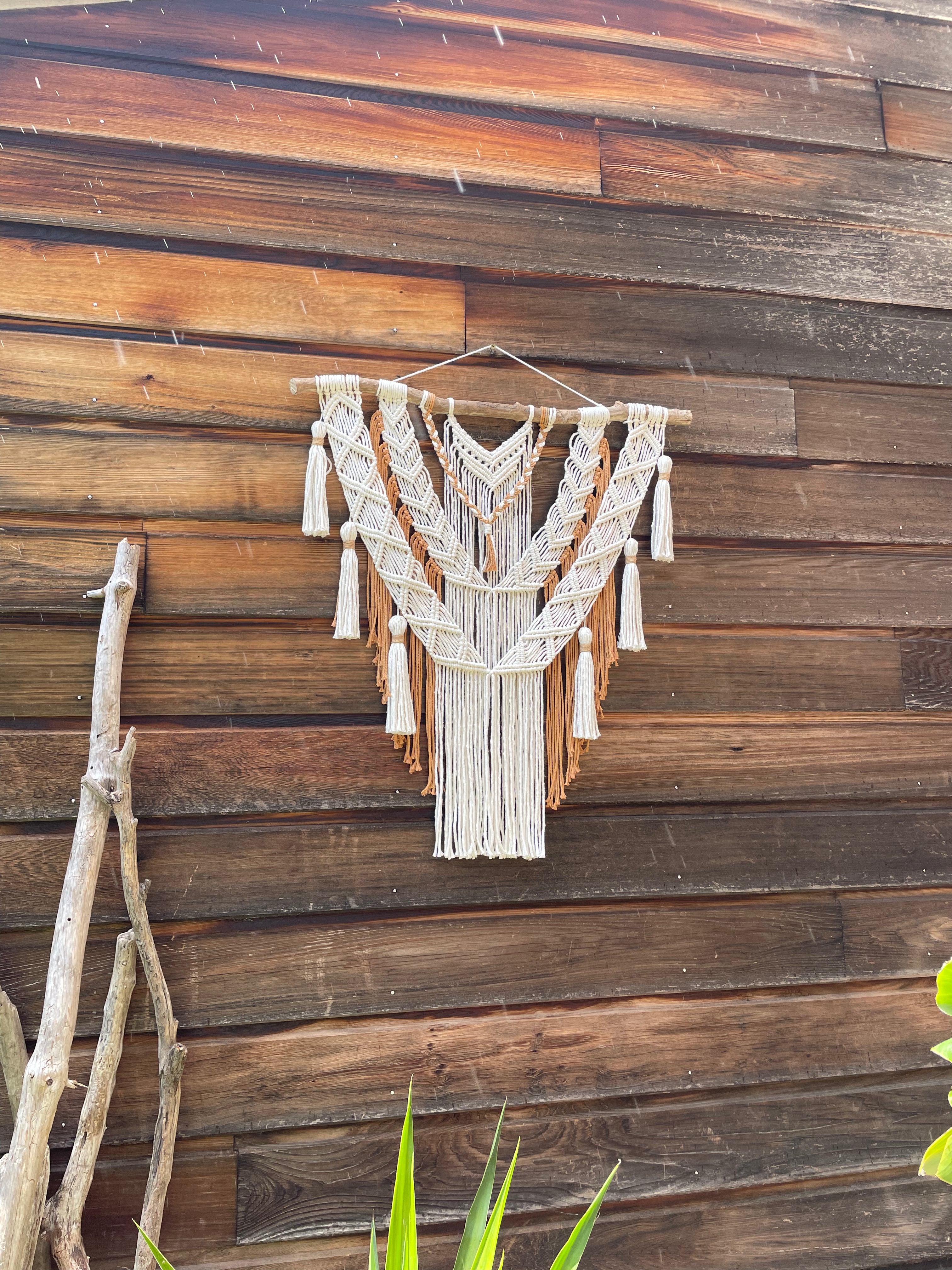 tenture murale bohème chic corde de coton blanc et beige marron tressé en technique macramé sur un bois flotté suspendu contre un mur