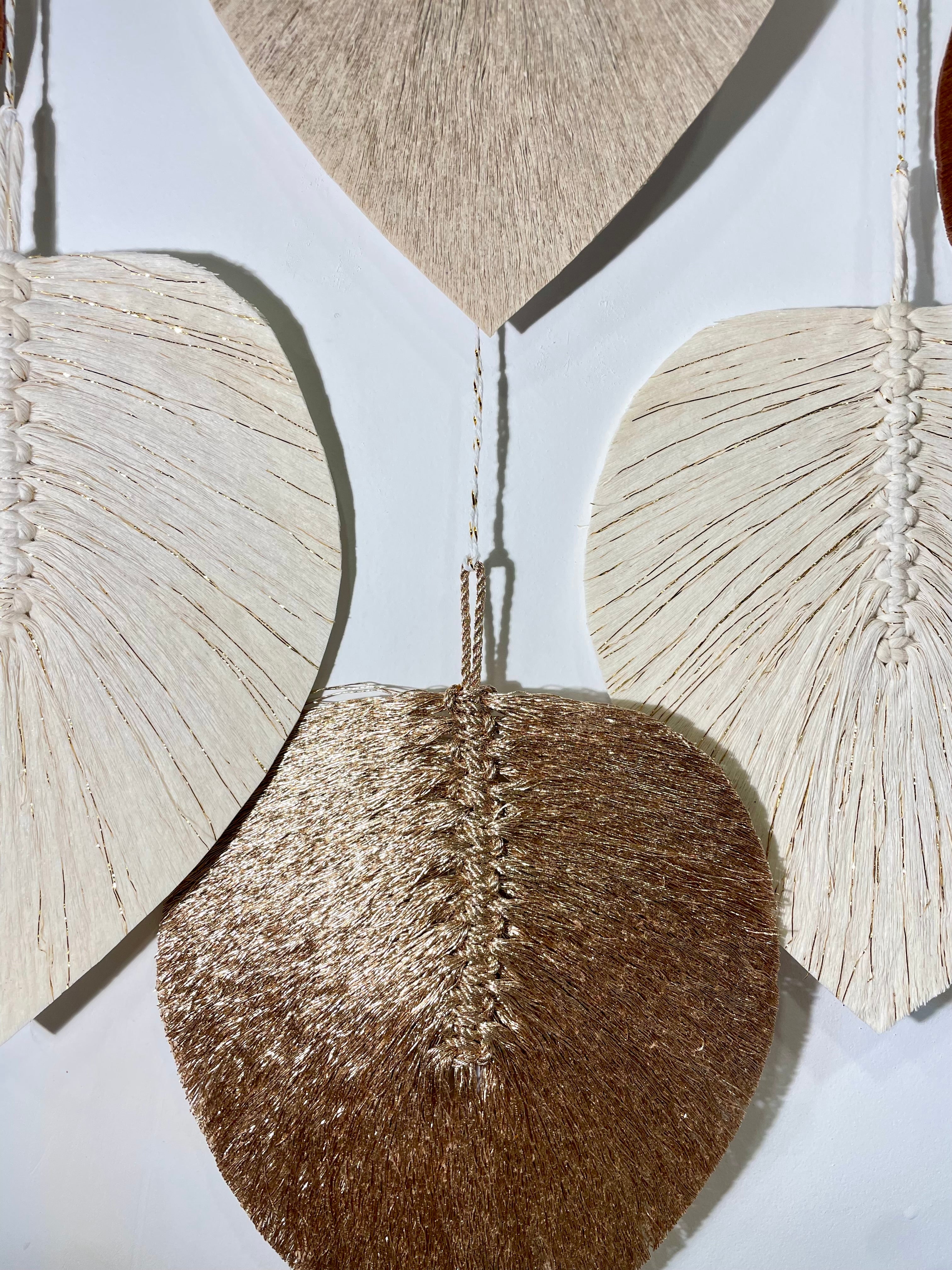 zoom sur des feuilles dorées en corde de coton stabilisée suspendues par un petit fil blanc et or
